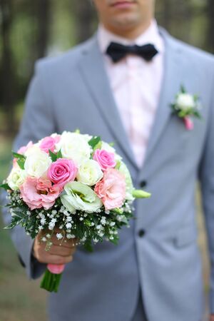 Young smiling groom wearing grey suit keeping bouquet of flowers. Concept of weddong photo session and floristic art.の写真素材