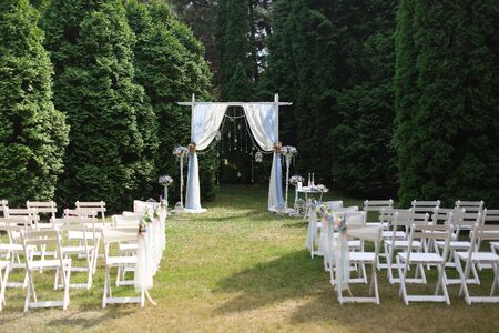 White wedding arch in park and decorated chairs. Concept of bridal decorations and elements.の写真素材