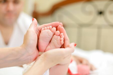 Mother hands with red nails holding little legs of newborn baby, father in background. Concept of babes and family.の写真素材