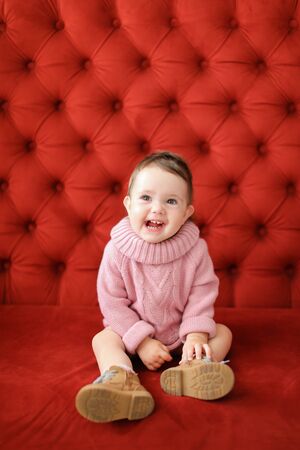 Little female baby sitting in red background on sofa. Concept of babias and photo session.の写真素材