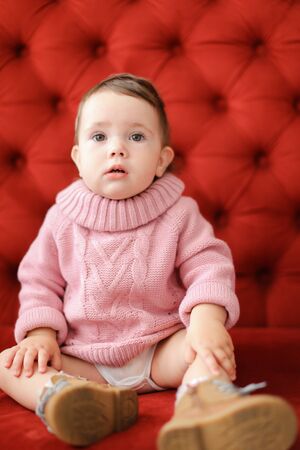 Little nice female baby sitting in red background on sofa. Concept of babias and photo session.の写真素材