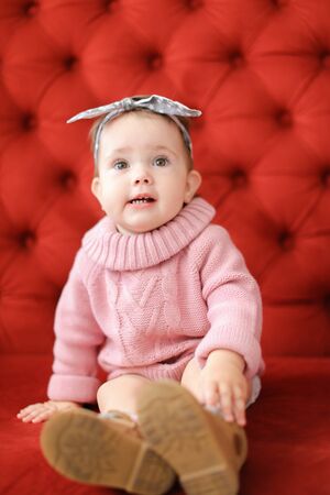 Little happy female baby sitting in red background on sofa. Concept of babias and photo session.の写真素材