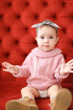 Little beautiful female baby sitting in red background on sofa. Concept of babias and photo session.の写真素材