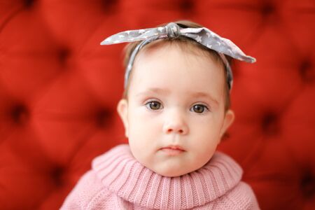 Closeup female baby wearing pink sweater sitting in red background. Concept of babies and photo session.の写真素材