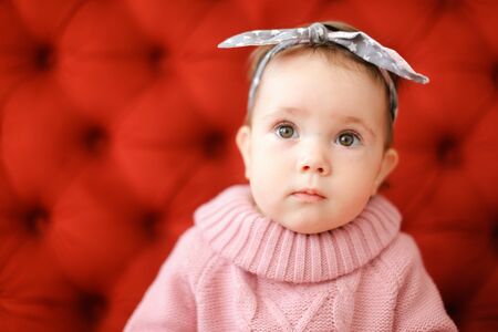 Closeup female child wearing pink sweater sitting in red background. Concept of babies and photo session.の写真素材