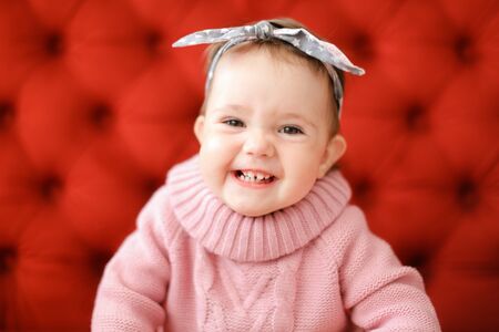 Closeup smiling female baby wearing pink sweater sitting in red background. Concept of babies and photo session.の写真素材