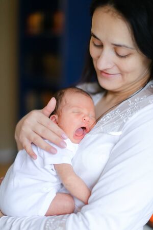 Young happy mother wearing white clothes holding newborn baby. Concept of motherhood and happiness.の写真素材