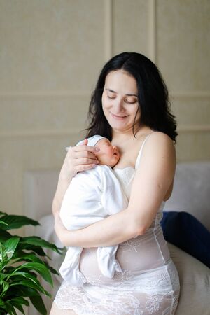 Young happy mother wearing white clothes holding newborn baby. Concept of motherhood and happiness.の写真素材