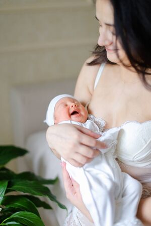 Young pretty mother wearing white clothes holding newborn baby. Concept of motherhood and happiness.の写真素材