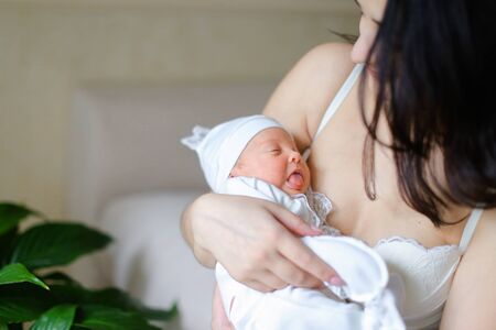 Black haired young woman holding newborn baby near green plant. Concept of motherhood and babies.の写真素材