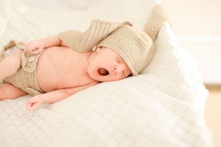Cute newborn baby yawning, sleeping and wearing crocheted clothes, white background. Concept of babies and new life.の写真素材