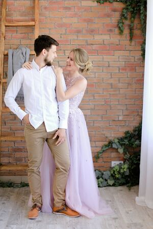 Groom and blonde bride standing with brick wall background. Concept of wedding and happy couple.の写真素材