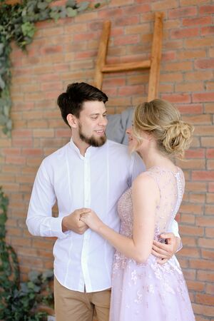Caucasian groom and blonde bride standing with brick wall background. Concept of wedding and happy couple.の写真素材