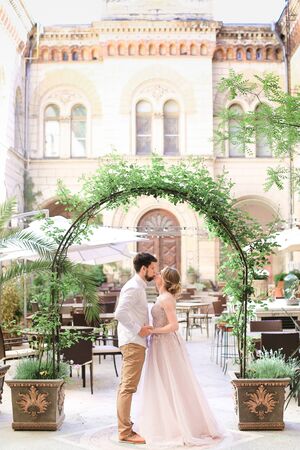 Groom and bride standing near arch at restaurant, building in background. Concept of wedding and happy couple.の写真素材