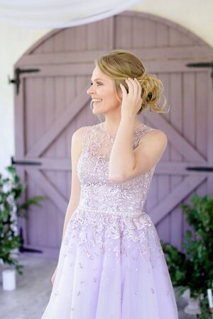 Beautiful blonde bride standing near wooden gate and wearing dress. Concept of wedding and fiancee photo session.の写真素材