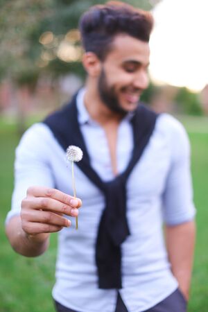 Blurred photo of hispanic male person blowing dandelion. Concept of male person in green background.の写真素材