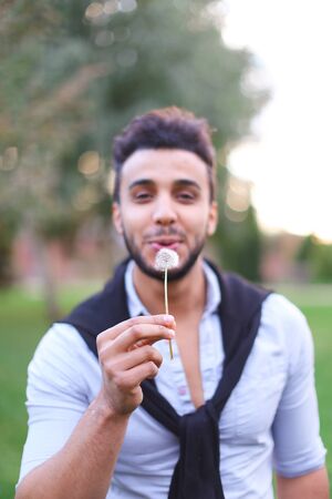 Young hispanic guy blowing dandelion. Concept of happines and spring.の写真素材