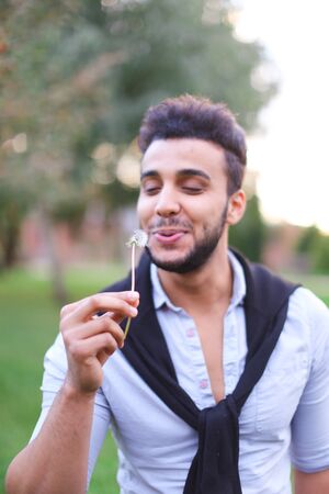 Young hispanic guy blowing dandelion. Concept of happines and spring.の写真素材