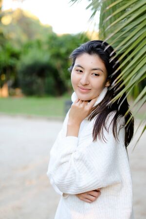 Chinese nice woman in white sweater standing near palm leaf. Concept of asian beauty and female person on tropical resort.の写真素材