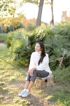 Japanese woman sitting on stump in park and wearing white sweater. Concept of asian female person.の写真素材