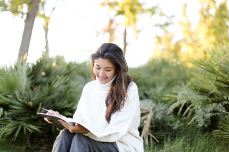Chinese happy female student sitting on stump in park and reading papers. Concept of preparing before exam and asian woman.の写真素材