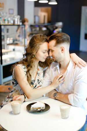 Young caucasian boy and girl sitting at cafe with cups of coffe, cake and hugging. Concept of happy couple and taking rest with lunch.の写真素材