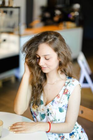 Young cute girl sitting at cafe and touching curly hair. Concept of happy female person and resting.の写真素材