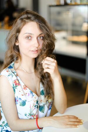 Young nice student sitting at cafe and touching curly hair. Concept of happy female person and resting.の写真素材