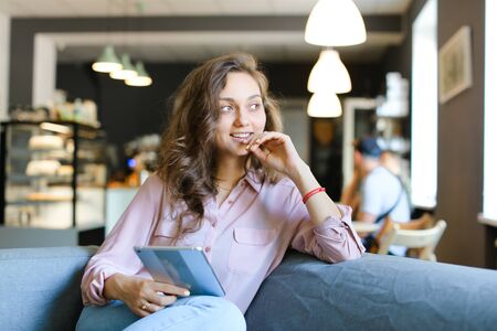 Young american woman enjoying with fast internet by tablet and sitting at cafe. Concept of free hotspot at catering establishment and spending time with modern technology.の写真素材