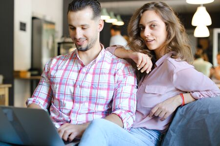 Young beautiful woman and man using laptop at cafe and surfing. Concept of free hotspot and fast internet, modern technology and happy couple.の写真素材
