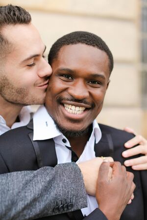 Portrait of caucasian man kissing afroamerican boy. Concept of gays and happy same sex couple.の写真素材