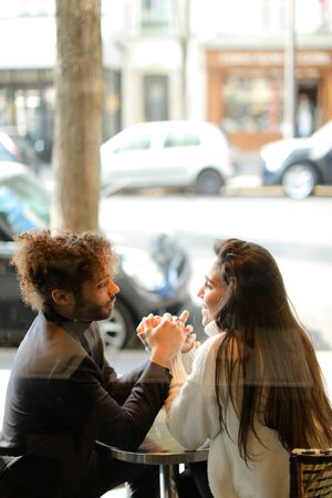 Afro american man and caucasian woman sitting at street cafe and holding hands, reflection in glass. Concept of international couple and love.の写真素材