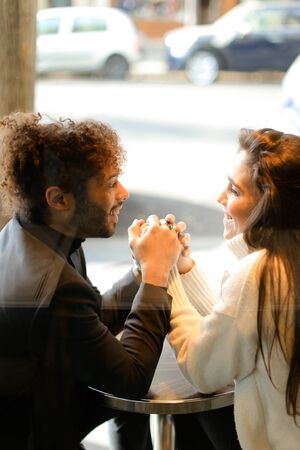 Afro american man and caucasian woman sitting at street cafe and holding hands, reflection in glass. Concept of international couple and dating.の写真素材