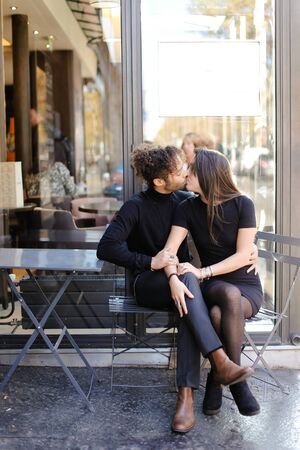 Afro american man sitting with caucasian woman and kissing outside. Concept of international couple and love.の写真素材