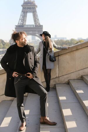 Focus on afro american man with curly hair on concrete stairs, girl and Eiffel Tower in background, Paris.の写真素材