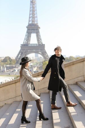 Afro american boy and caucasian girl holding hands and walking on stairs, Eiffel Tower in background, Paris.Concept of love and international couple, vacations in France.の写真素材