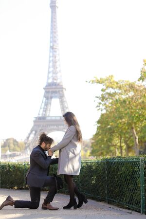 Afro american man making proposal to caucasian girlfriend in Paris, Eiffel Tower in background. Concept of love and international couple.の写真素材