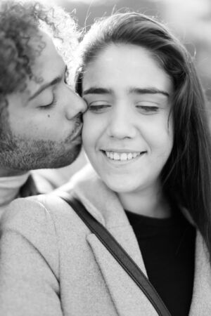 Black and white photo of afro american man kissing caucasian pretty girlfriend outside. Concept of international couple and love.の写真素材