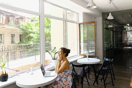 Young european woman wearing dress and sitting with laptop at cafe. Concept of social networks and fast internet.の写真素材