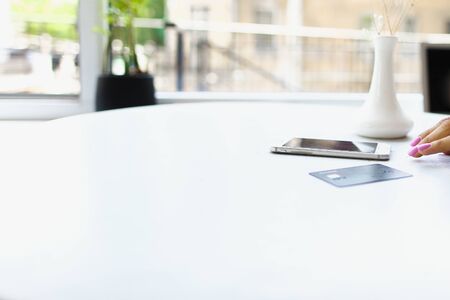 Smartphone and credit card lying on white table near female hand. Concept of purchasing online.
