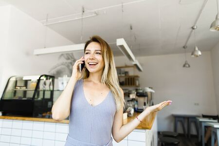 Blonde housewife standing in kitchen and talking by smartphone. Concept of happy wife and modern technology.の写真素材