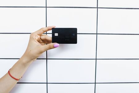 Female hands holding debit card in white tile wall background. Concept of bank account and credit.の写真素材