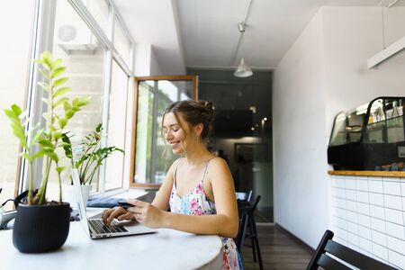 Young woman holding credit card and typing by laptop at cafe. Concept of buying goods online and shopping by internet.の写真素材