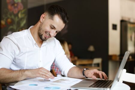 Young businessman working with documents and laptop at cafe, wearing white shirt. Concept of business and job, modern technology.の写真素材