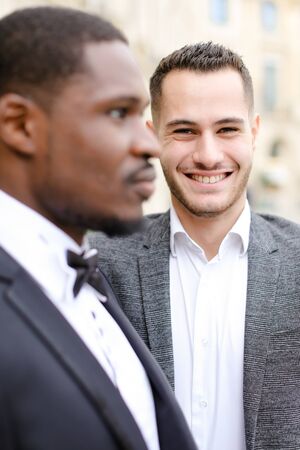 Focus on caucasian man wearing suit standing near afro american guy. Concept of business and male fashion.の写真素材
