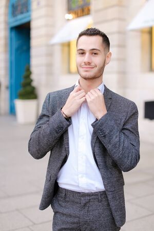 Young cacuasian male person wearing suit and wite shirt standing near building outdoors. Concept of fashion and businessman, urban life.の写真素材