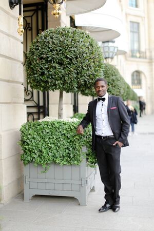Afro american happy good looking male person wearing suit and standing near tree in city. Concept of black businessman.の写真素材