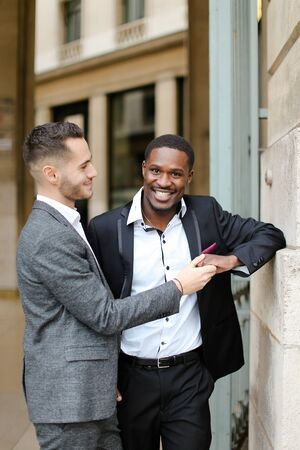Caucasian man hugging handsome afro american guy outside and wearing suit. Concept of happy same sex couple and gays.の写真素材