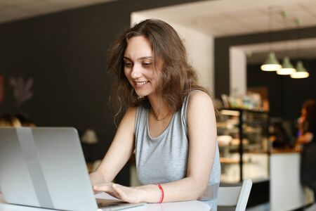 Young smiling girl making video call by laptop at cafe. Concept of social netwrorks and modern technology.の写真素材