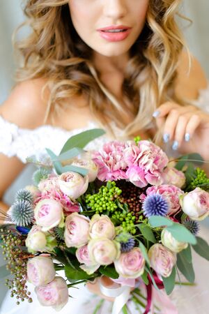 Young european bride wearing white dress with bouquet at photo studio. Concept of bridal photo session, wedding and floristic art.の写真素材